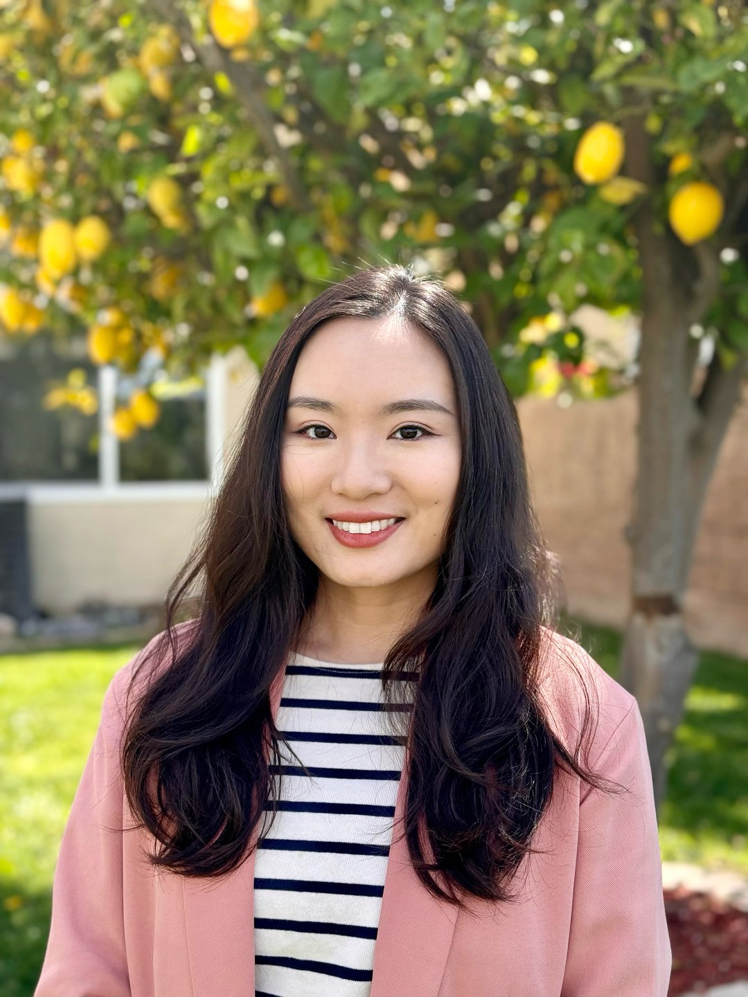Dongming Zhao, LCSW, standing outdoors beneath a lemon tree.